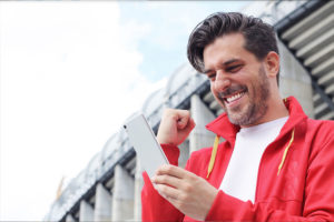 A man fist pumps his big sports betting win outside a stadium. He learned his sports betting strategy from Refund Management Services.